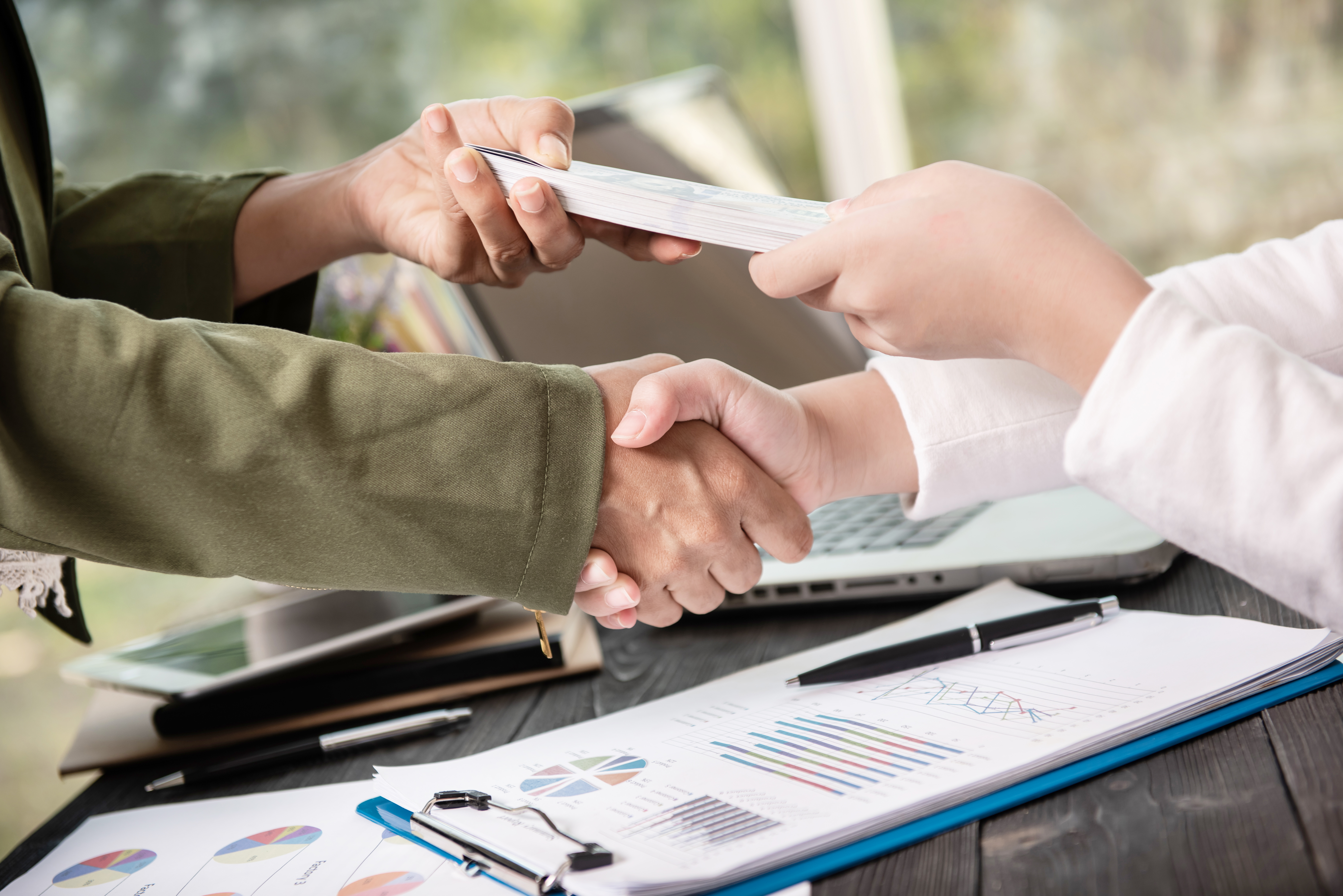 Business handshake and cash handoff with loan paperwork and charts—borrow smarter, faster, and stress-free